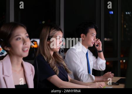 Groupe de courtiers négociants internationaux portant casque travaillant activement la nuit dans le bureau, concept de l'âge du support client Banque D'Images