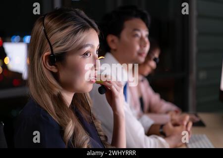 Groupe de courtiers négociants internationaux portant casque travaillant activement la nuit dans le bureau, concept de l'âge du support client Banque D'Images