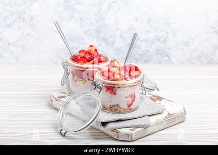 Parfait avec fraises fraîches, yaourt et granola Crunchy en verre transparent Mason pots sur fond blanc rustique en bois A Banque D'Images