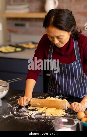 Femme asiatique concentrée faisant cuire la pâte à rouler dans la cuisine Banque D'Images