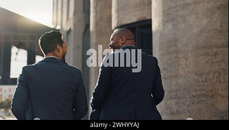 Affaires, hommes et voyage en ville avec discussion pour le trajet matinal, partenariat et vue arrière avec lumière parasite. Employés, personnes et parler pour Banque D'Images