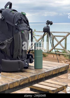 Sac à dos photo et thermos reposent sur la table devant l'appareil photo Banque D'Images