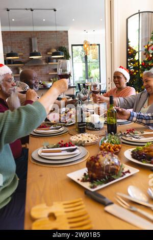 Heureux groupe diversifié d'amis seniors toast au dîner de noël dans la salle à manger ensoleillée à la maison Banque D'Images