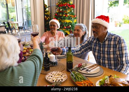 Heureux groupe diversifié d'amis seniors toast au dîner de noël dans la salle à manger ensoleillée à la maison Banque D'Images