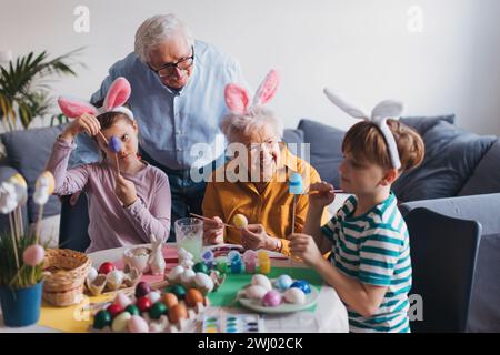 Grand-mère avec de petits enfants décorant des œufs de pâques à la maison. Tradition de peindre les oeufs avec pinceau et colorant d'oeuf de pâques. Banque D'Images