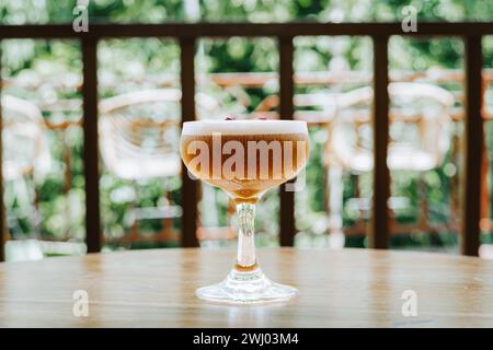 Gros plan d'un verre de cocktail de café avec dessus mousseux et boutons de rose séchés supplémentaires sur la table en bois Banque D'Images