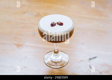 Gros plan d'un verre de cocktail de café avec dessus mousseux et boutons de rose séchés supplémentaires sur la table en bois Banque D'Images