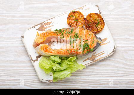 Poisson grillé saumon steak et salade verte avec citron servi sur planche à découper blanche fond en bois rustique vue de dessus, équilibré d Banque D'Images