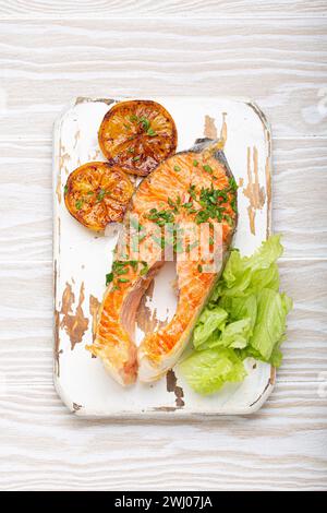 Poisson grillé saumon steak et salade verte avec citron servi sur planche à découper blanche fond en bois rustique vue de dessus, équilibré d Banque D'Images