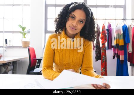 Créateur de mode féminin biracial concentré ayant un appel vidéo au bureau dans le studio. Mode, design, créativité, vêtements et petites entreprises, communication, Banque D'Images