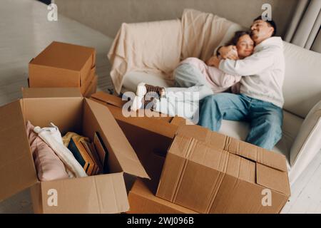 Heureux jeune couple de famille homme et femme se relaxant sur le canapé après avoir déplacé des boîtes en carton à l'appartement de la maison neuve Banque D'Images