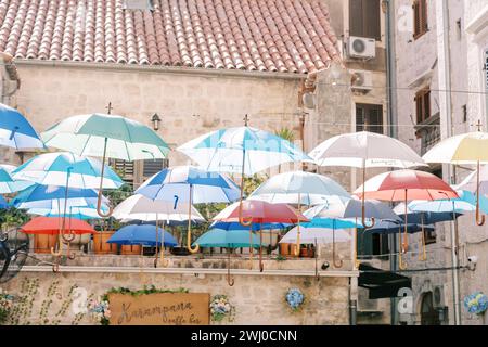 Des parapluies colorés accrochent sur des cordes au-dessus de la rue près d'une ancienne maison en pierre Banque D'Images