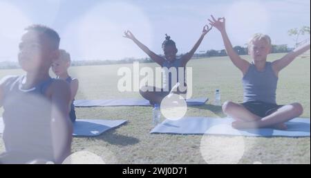 Image de taches de lumière blanche au-dessus de divers écoliers heureux faisant du yoga en classe en plein air Banque D'Images