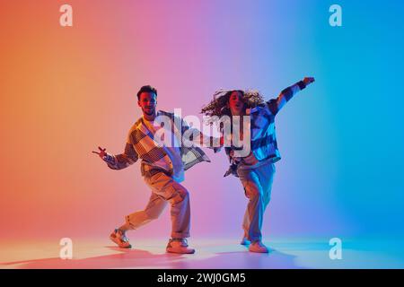 Couple dansant se déplace en synchronisation, homme et femme, dansant dans un studio éclairé au néon sur fond dégradé. Expression énergétique. Style urbain. Banque D'Images