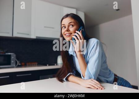 Jeune femme parlant sur le téléphone portable tout en se tenant debout dans la cuisine avec four à micro-ondes en arrière-plan Banque D'Images