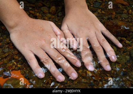 La main qui est mise dans l'eau coule dans la rivière. Banque D'Images