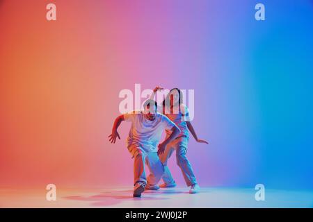 Style de vie dynamique. Danseurs réalisant du hip hop, du freestyle dans des néons sur fond de studio dégradé. Banque D'Images