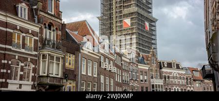 Façade extérieure de maisons de canal hollandaises authentiques avec tour de cathédrale montante derrière dans un échafaudage Banque D'Images