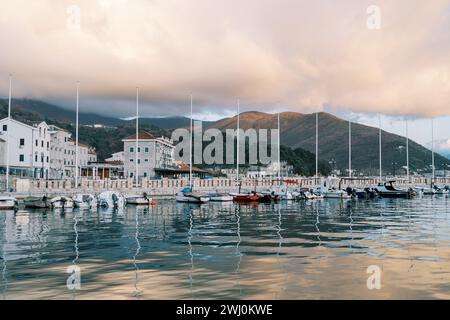 Les yachts à voile se dressent en rangée sur la jetée avec des villas colorées au pied des montagnes dans les reflets du coucher du soleil Banque D'Images