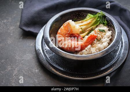 Crevettes géantes frites ou crevettes avec riz et pak choi dans un bol en céramique noir tacheté sur fond sombre, cuisine dans le style asiatique, Banque D'Images