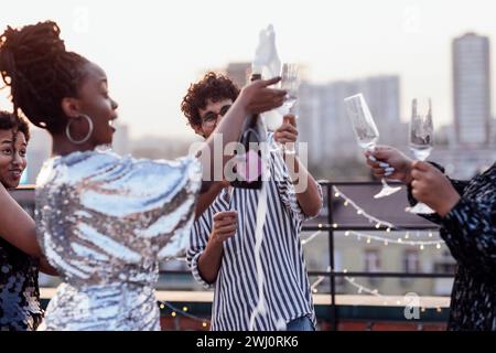 Une fille à la peau foncée verse du champagne dans les verres de ses amis multinationaux Banque D'Images