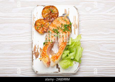 Poisson grillé saumon steak et salade verte avec citron servi sur planche à découper blanche fond en bois rustique vue de dessus, équilibré d Banque D'Images