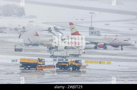 während ein Airbus A320-271N von Swiss International Airlines und ein Flugzeug von Austrian Airlines enteist werden. Fahren vorne Schneepflüge durch. Banque D'Images