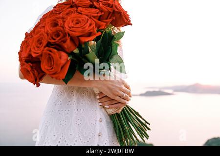 Énorme bouquet de roses rouges dans les mains d'une femme avec une bague de fiançailles sur son doigt. Rogné. Sans visage Banque D'Images