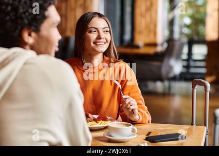 Jeune femme souriante ayant un délicieux petit déjeuner avec petit ami dans un café confortable Banque D'Images