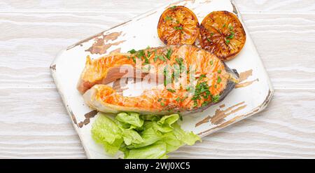 Poisson grillé saumon steak et salade verte avec citron servi sur planche à découper blanche fond en bois rustique vue de dessus, équilibré d Banque D'Images