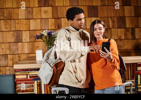couple heureux diversifié partageant moment de joie comme ils regardent l'écran de smartphone dans l'auberge Banque D'Images