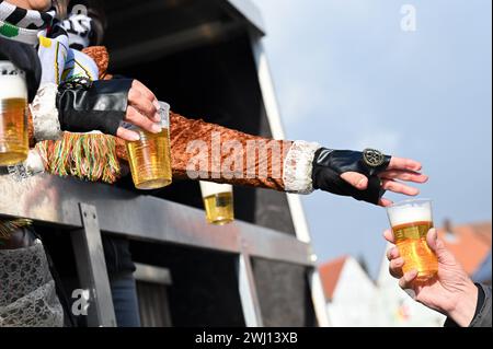 Herbstein, Allemagne. 12 février 2024. Les tasses de bière remplies sont distribuées à partir d'un flotteur pendant le Herbstein Springerzug. Les tailleurs de pierre tyroliens ont apporté la tradition à Herbstein au XVIIe siècle. Plus de 50 chars ont pris part au traditionnel défilé Rose Monday dans la ville du district de Vogelsberg. Crédit : Uwe Zucchi/dpa/Alamy Live News Banque D'Images
