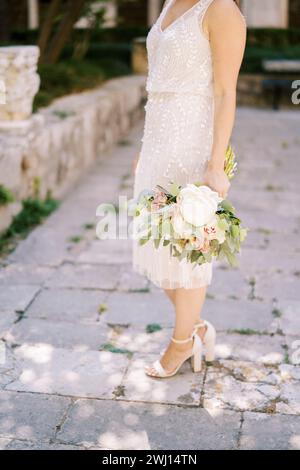 Mariée avec un bouquet de fleurs se tient à moitié tourné sur les pavés. Rogné. Sans visage Banque D'Images