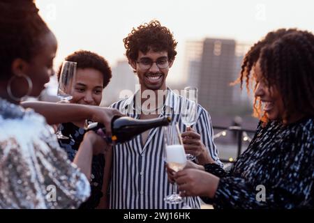 Une fille à la peau foncée verse du champagne dans les verres de ses amis multinationaux Banque D'Images