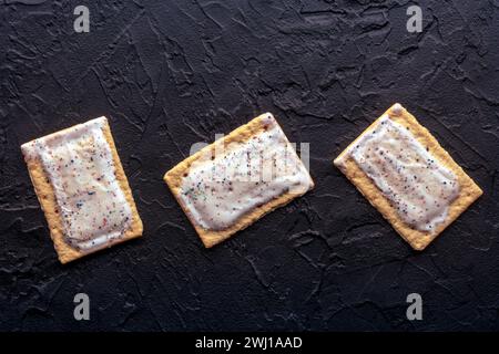 Tartes pop. Pâte grille-pain Poptart avec glaçage sur un fond noir, plan de pose à plat suspendu avec un endroit pour le texte Banque D'Images