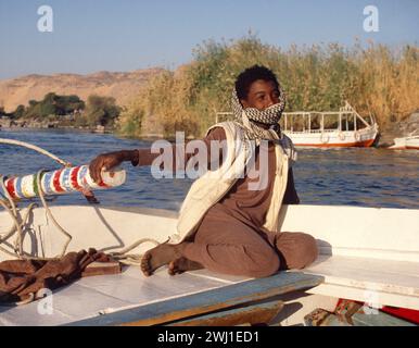 Égypte. Assouan. Garçon nubien à Tiller of Felucca voilier sur le Nil. Banque D'Images