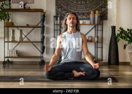 Homme adulte faisant Ardha Padmasana avec Gyan mudra pendant la méditation pleine conscience à la maison Banque D'Images