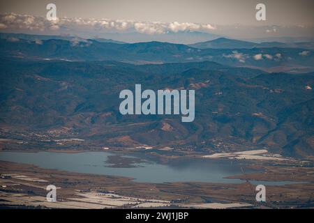 Une perspective aérienne à couper le souffle capture des montagnes majestueuses encerclant un lac serein, avec des collines douces à proximité Banque D'Images