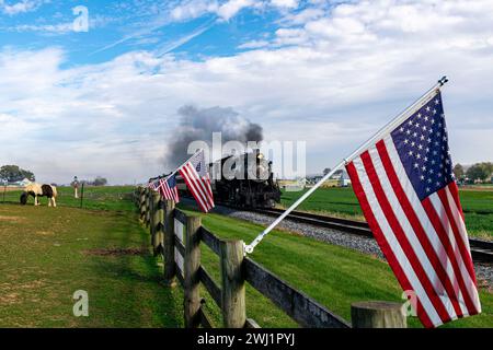 Vue d'un train de passagers à vapeur antique approchant avec une ligne de drapeaux américains Banque D'Images