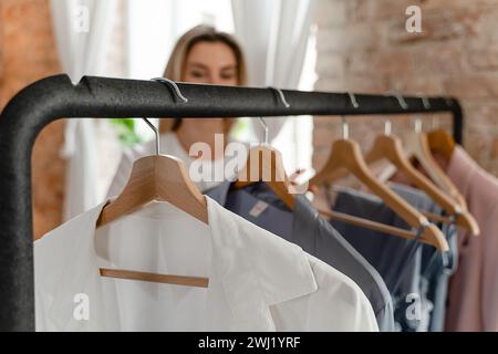 Femme parcourt ses diverses tenues accrochées sur le porte-vêtements dans sa garde-robe Banque D'Images