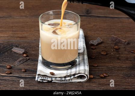 Verser la liqueur de crème irlandaise originale dans un verre avec de la glace. Fond en bois, espace de copie. Banque D'Images