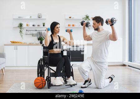 Physiothérapeute montrant à une femme adulte en fauteuil roulant comment faire des exercices. Banque D'Images