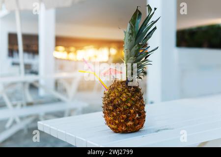 Cocktail tropical servi à l'ananas sur une table blanche au coucher du soleil Banque D'Images