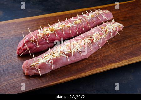 Filet de porc cru Mangalica farci de noix hachées et de citrouille offert en gros plan sur une planche à découper design en bois Banque D'Images