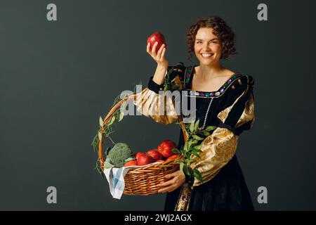 Portrait d'une jeune femme adulte vêtue d'une robe médiévale tenant un panier avec des légumes et des fruits. Récolte et foo sain Banque D'Images