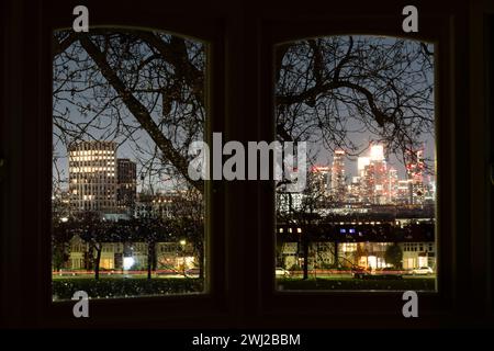 Vu à travers une baie vitrée d'une maison résidentielle et les branches d'arbres sont les fenêtres éclairées des maisons d'époque en terrasses bordant le parc Ruskin de Lambeth, et au loin un nouveau développement de tour à Higgs Yard à Loughborough Junction (à gauche) et le développement à Nine Elms (à droite), le 11 février 2024, à Londres, en Angleterre. Banque D'Images