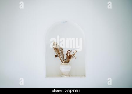 Fleurs séchées disposées dans un vase blanc dans une alcôve voûtée méditerranéenne. Décoration minimaliste. Banque D'Images