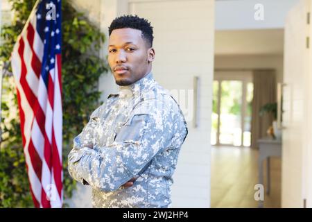 Soldat masculin afro-américain debout avec les bras croisés à l'extérieur de la maison et drapeau américain, copie espace Banque D'Images