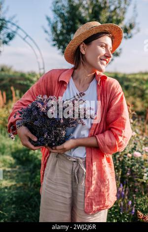 Récolte de lavande. Jeune jardinier tenant panier avec herbe coupée. Femme a cueilli un bouquet de fleurs violettes dans le jardin de roses d'été Banque D'Images