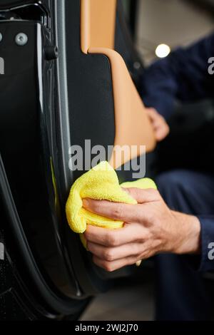 vue rognée d'un technicien professionnel dédié dans une voiture de nettoyage uniforme bleu avec chiffon jaune Banque D'Images